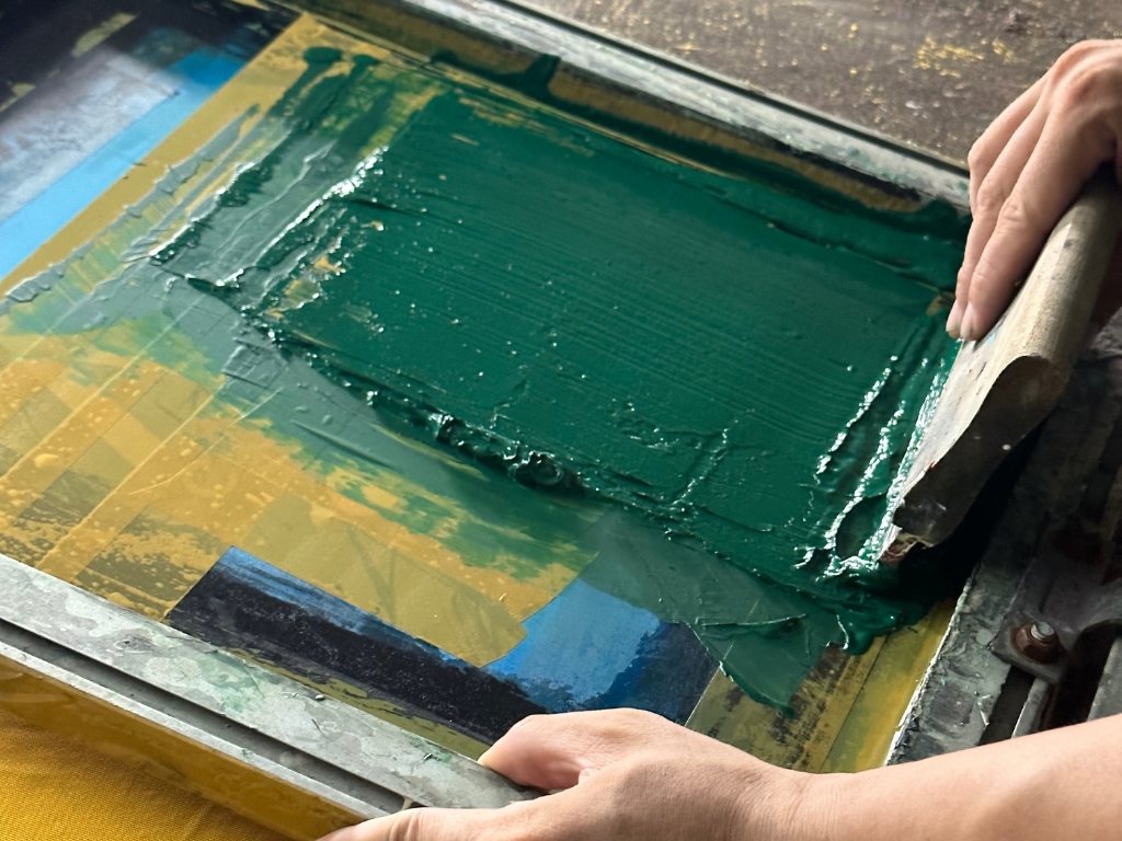 Thợ in kéo dao gạt mực để đẩy mực qua các mắt lưới và thấm xuống về mặt vải